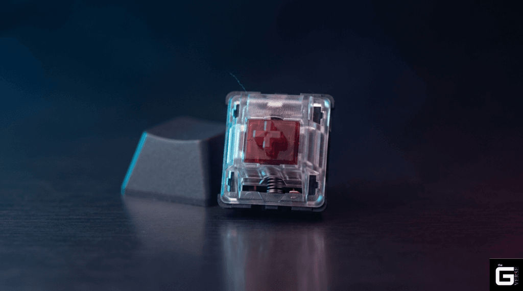 Clear keyboard switch housing with a red stem standing beside its keycap